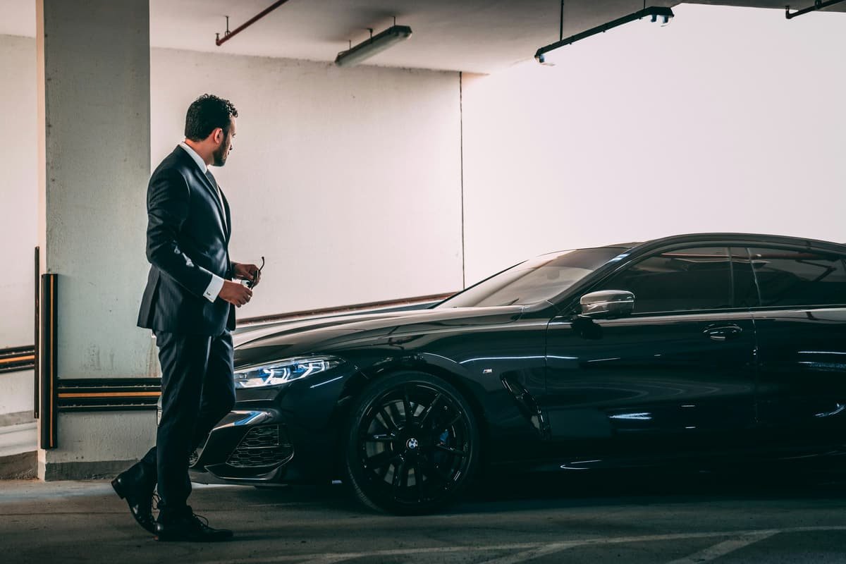 A man in a suit walking towards a black sedan